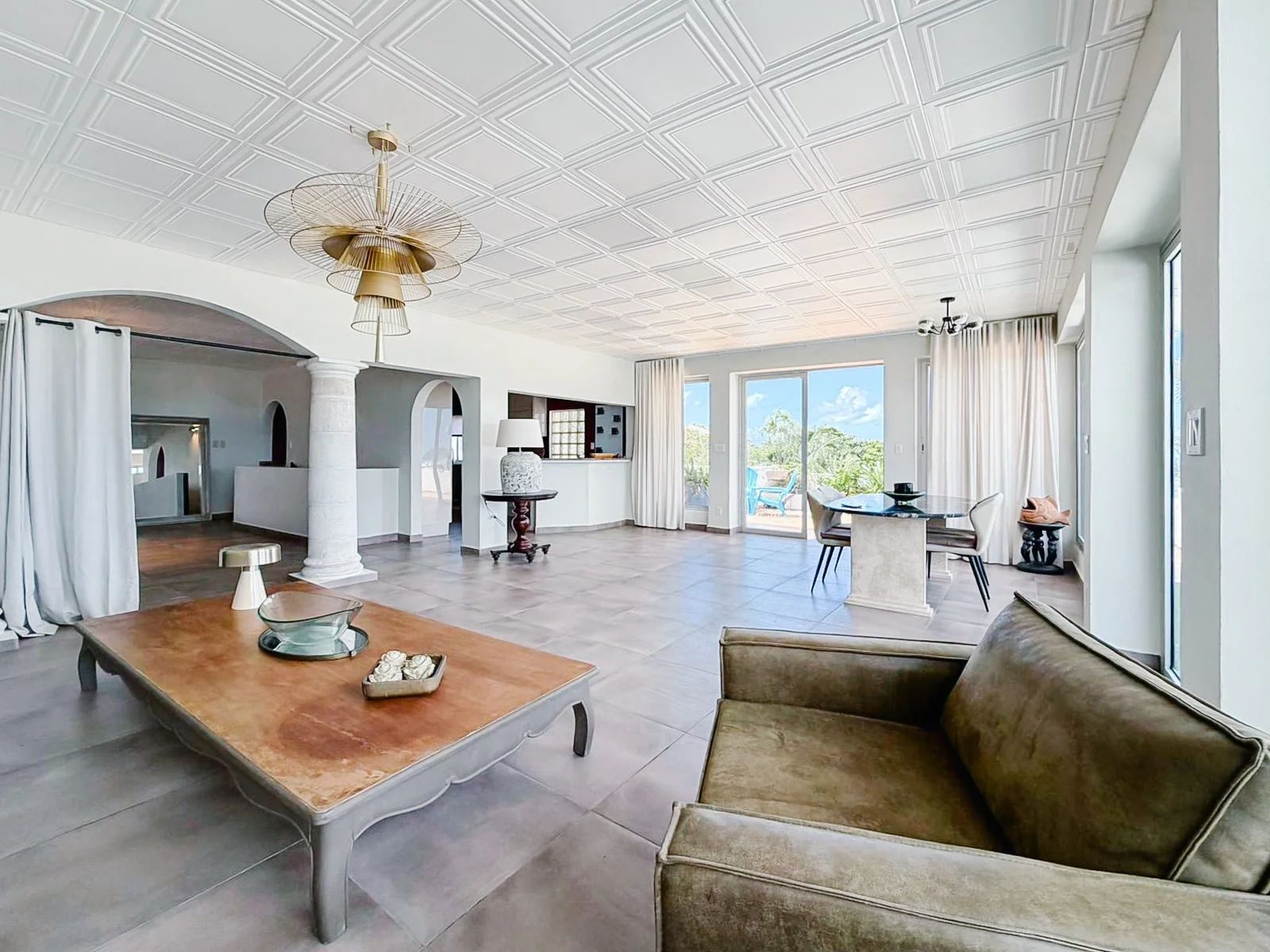 Open living area with classical columns, gold pendant chandelier and olive velvet sofa