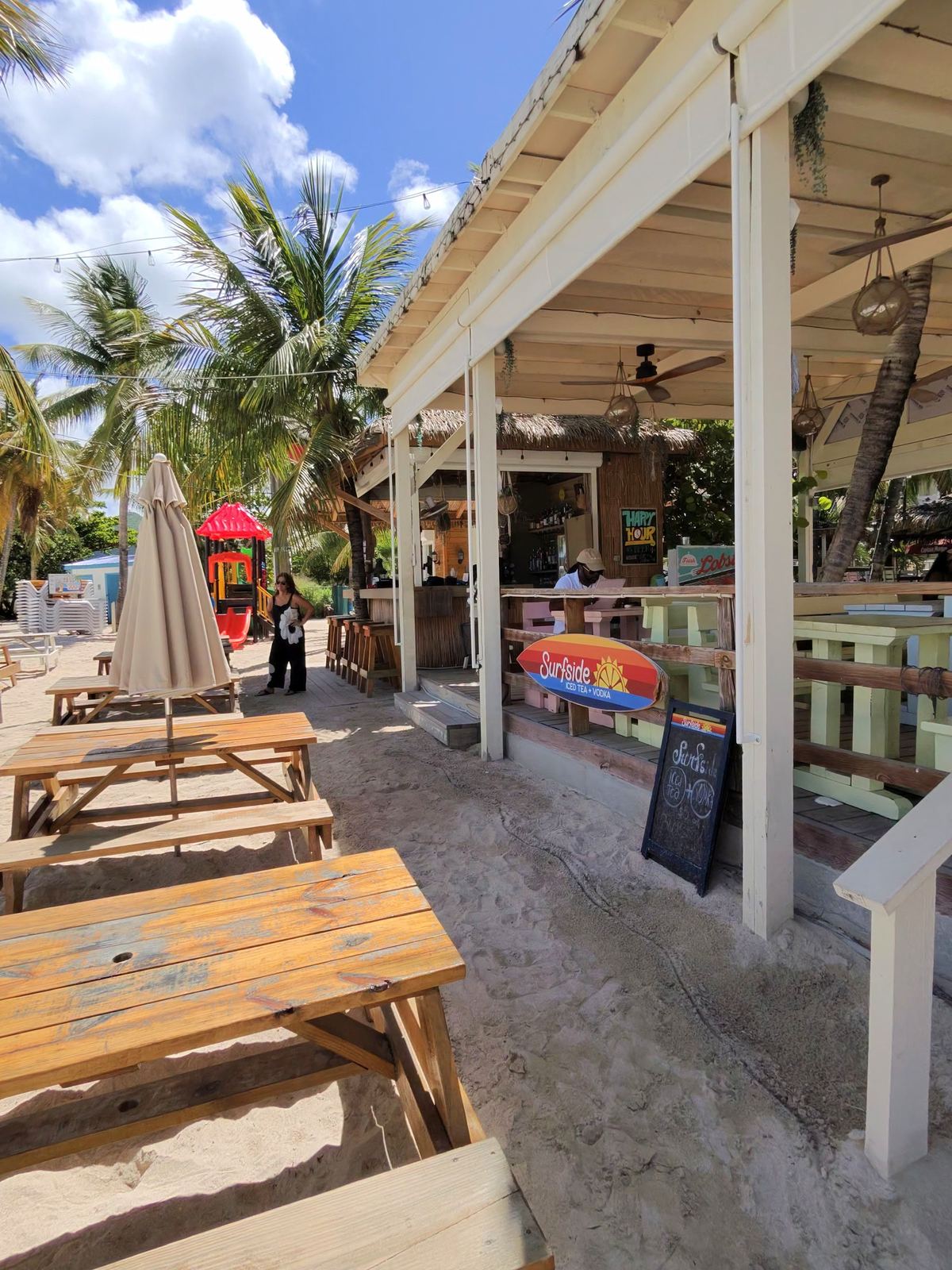 Beach bar with picnic tables in the sand under palm trees